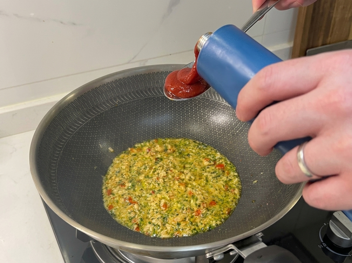 Tomato passata being poured into a pan containing sautéed tuna and aromatics.