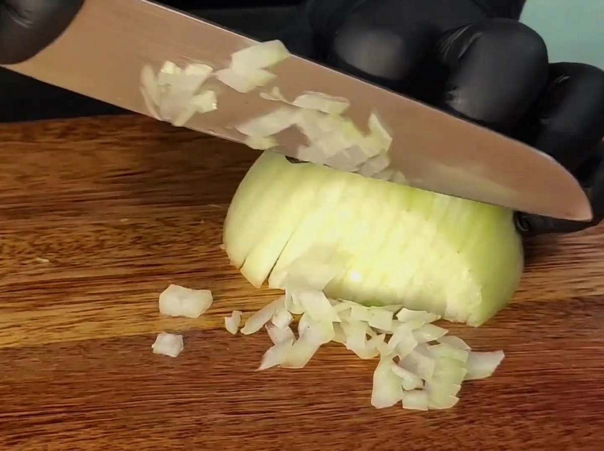 A knife slicing an onion on a wooden cutting board.