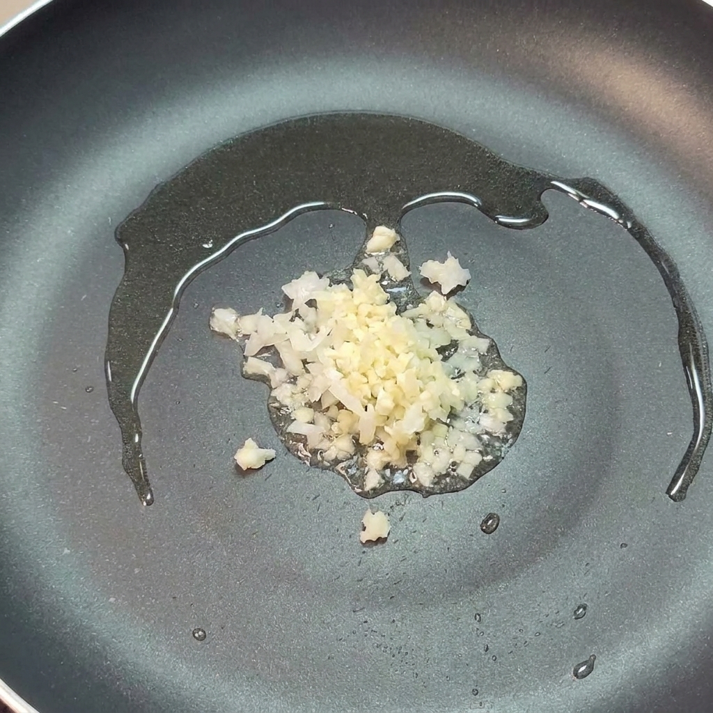 Minced onion and garlic sizzling in a bit of olive oil in a dark frying pan.