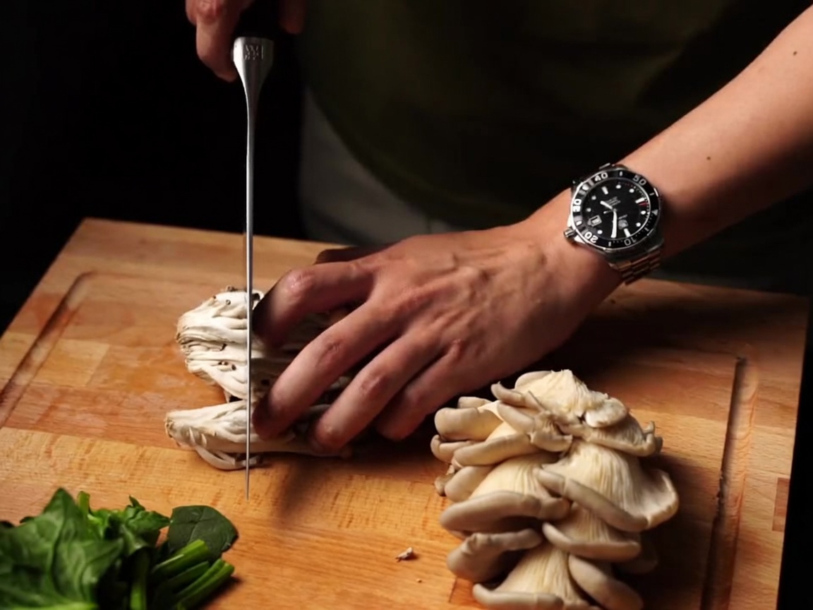 Fresh mushrooms being sliced with a knife on a wooden board.