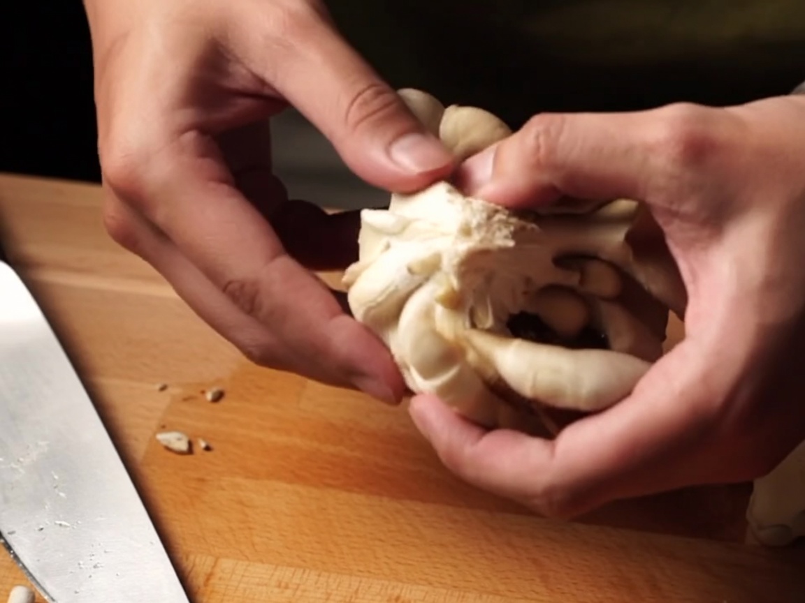 Hands tearing fresh mushrooms into smaller chunks.