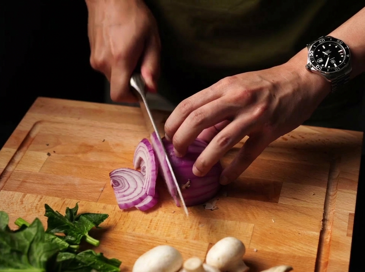 Red onion being thinly sliced on a wooden cutting board.