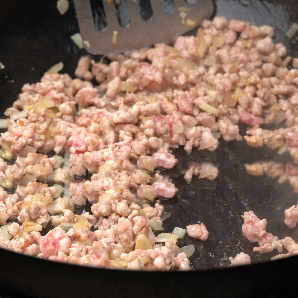 Minced meat browning in a pan alongside diced onions, being stirred.