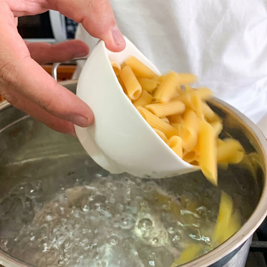 A close-up of a poached egg being placed in the center of a bowl of creamy penne pasta.