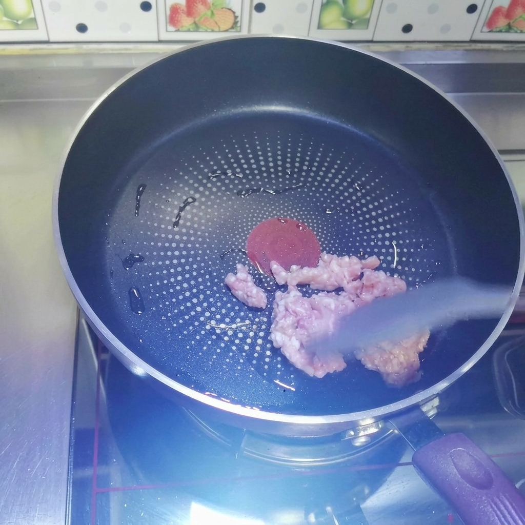 Raw minced meat being stir-fried in a heated dark non-stick pan with a grey silicone spatula.