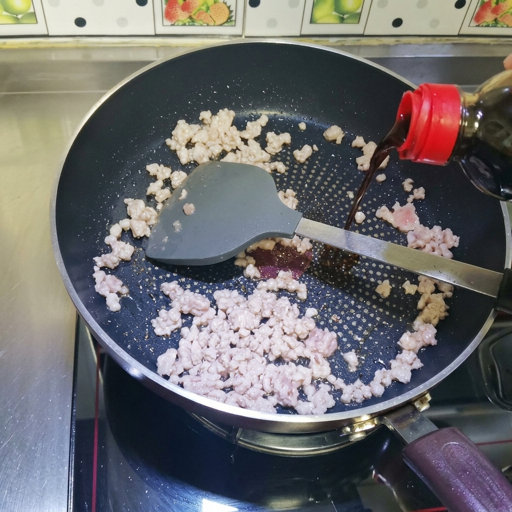 Dark liquid soy sauce being poured from a bottle over browned minced meat in a heated non-stick pan.