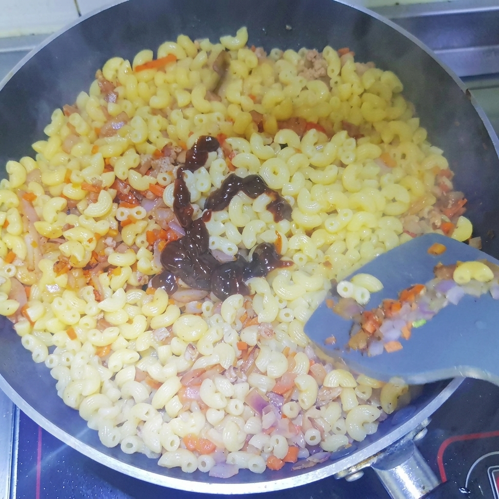 Dark black pepper sauce being squeezed in a spiral pattern over cooked macaroni in a pan.