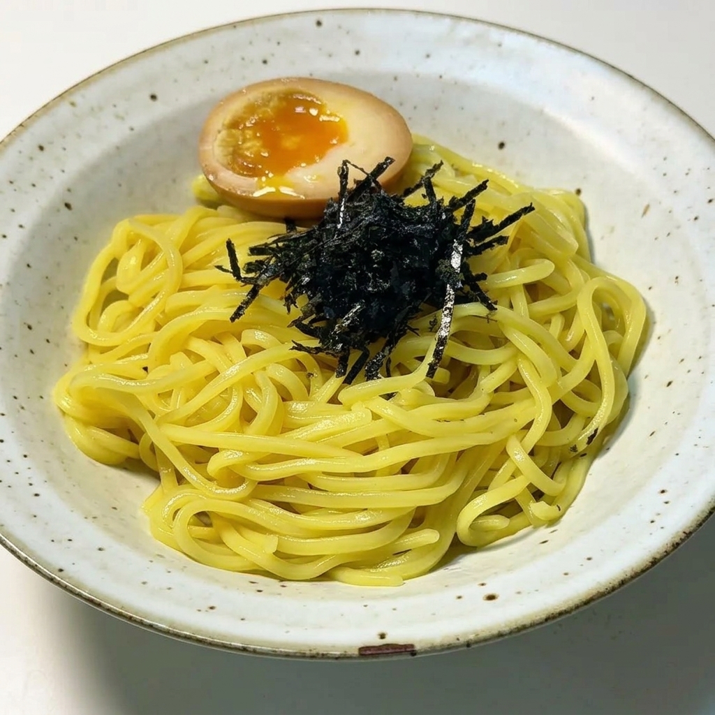 Plated ramen noodles topped with a neat pile of shredded black seaweed and a perfectly halved soft-boiled egg with a runny orange yolk.