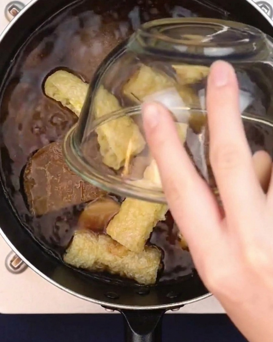 Fried tofu puffs being dropped into a pot of simmering Japanese curry broth.