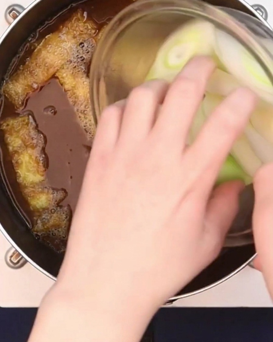 Diagonally sliced large green onions being added to a simmering curry broth.