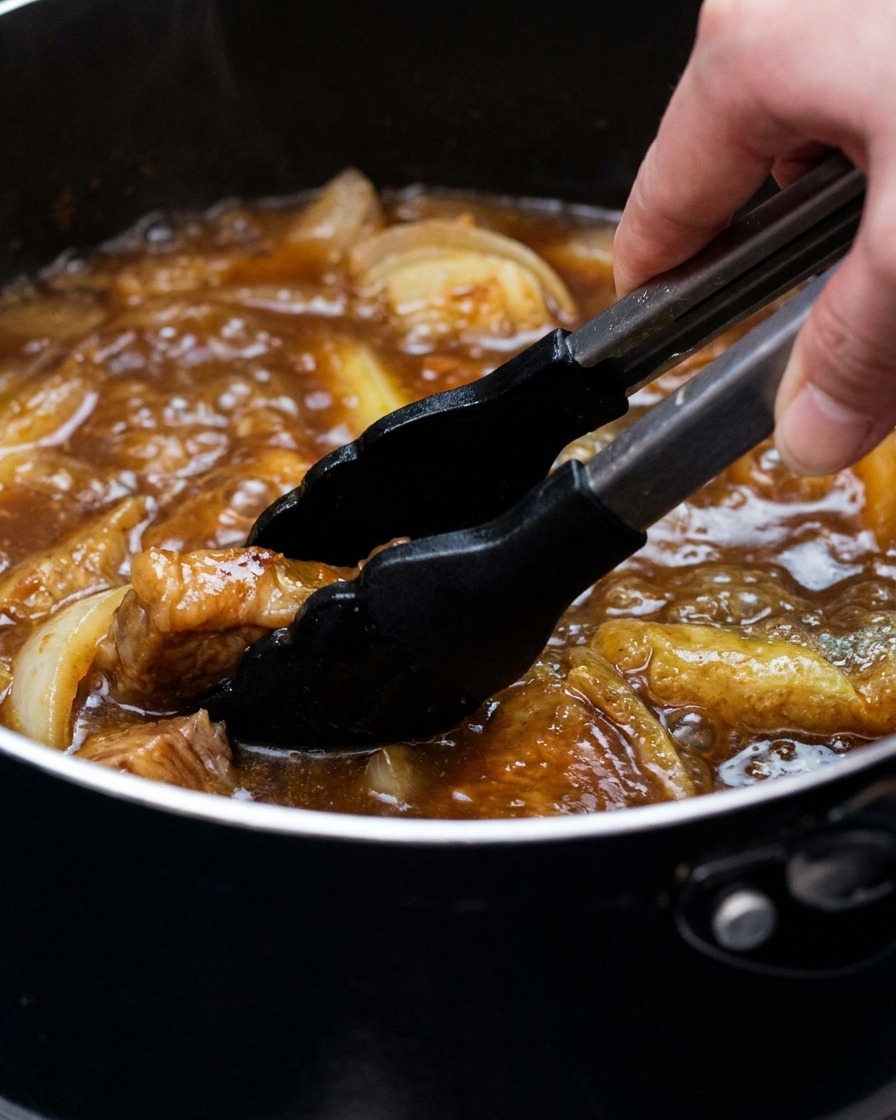 A pot of curry broth with tofu and green onions being stirred with tongs.