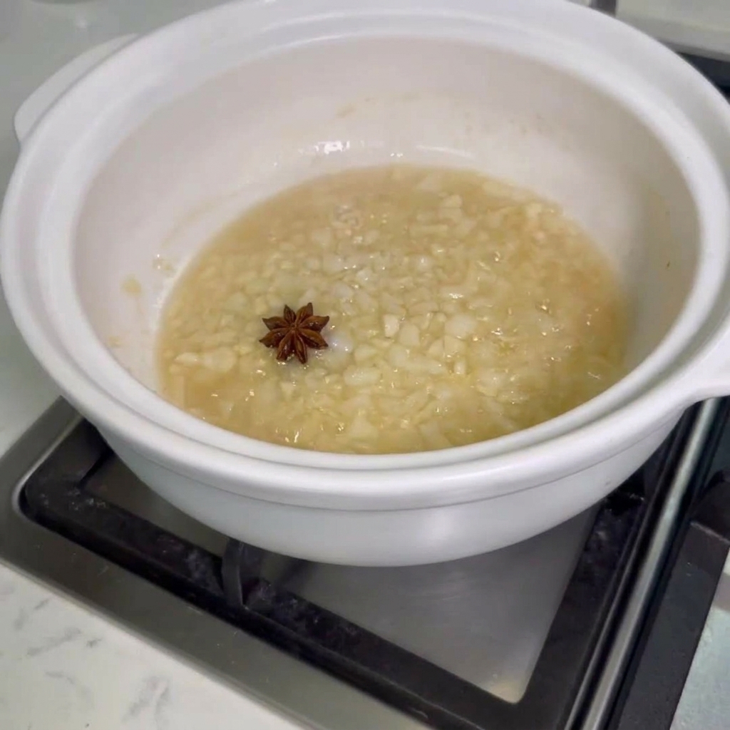 Star anise and raw chicken wings being added to a pot with sauteed onions and garlic.