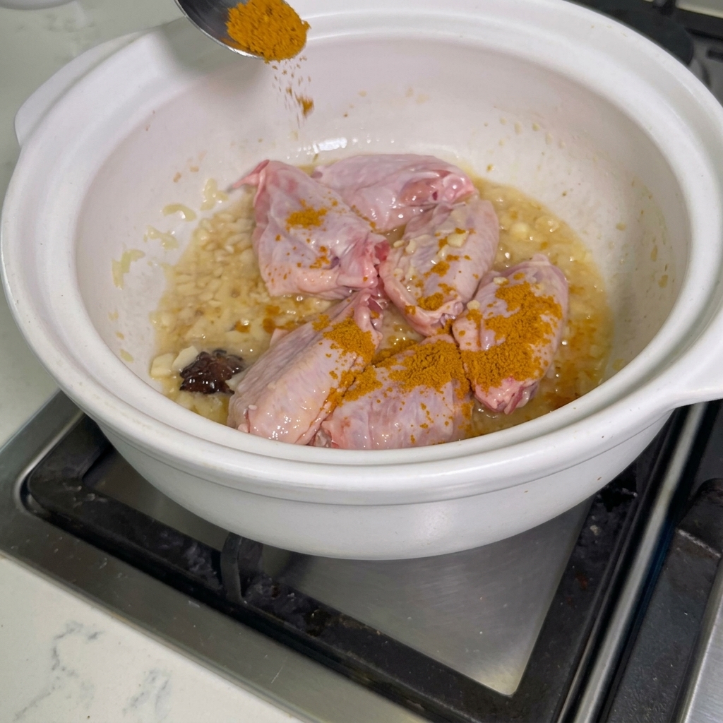Curry powder being sprinkled over chicken wings in a pot.