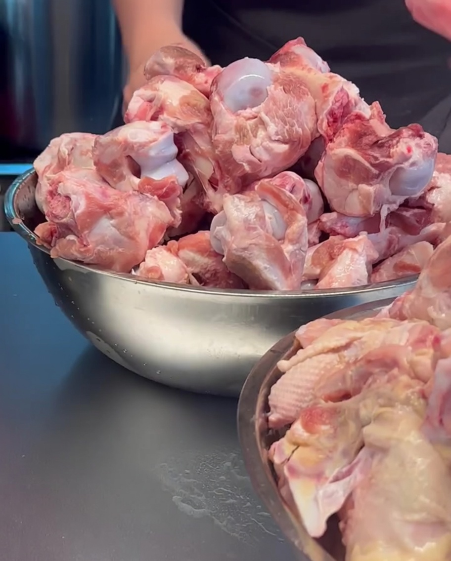 Raw pork bones and chicken carcasses being loaded into a large metal pot.