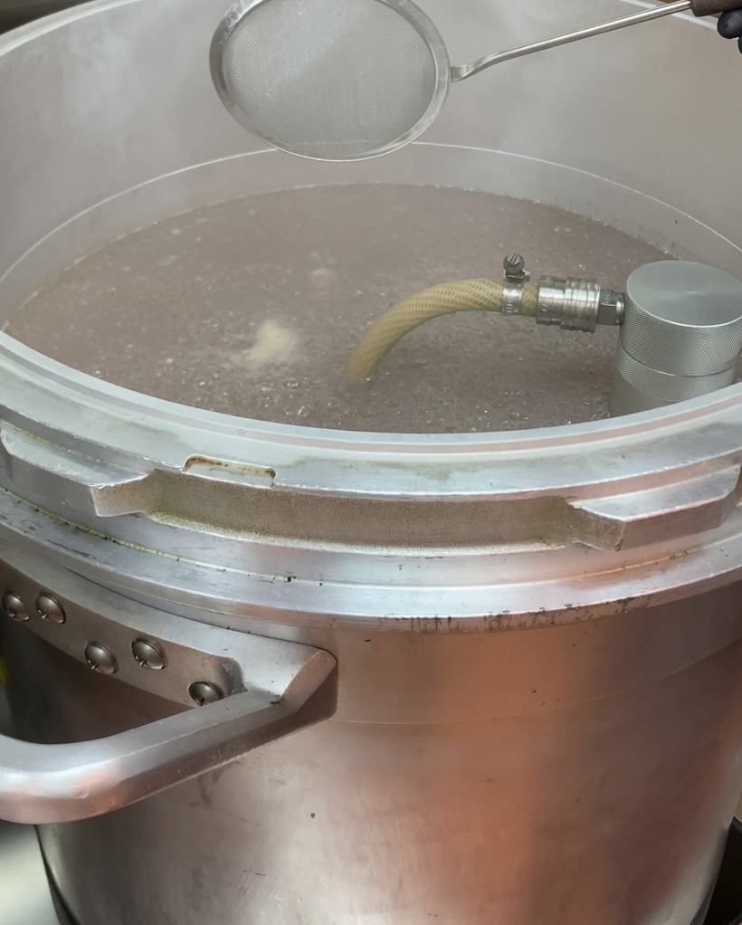 Removing foam from the surface of simmering broth using a mesh skimmer.