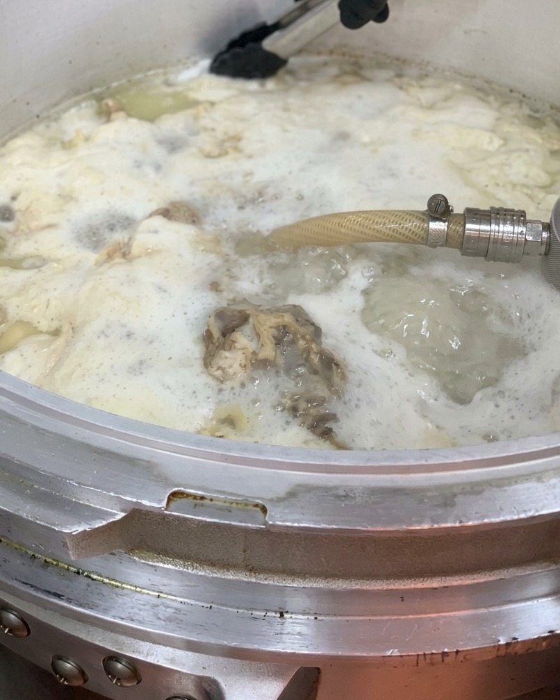 Chicken oil being poured into the large pot of broth.