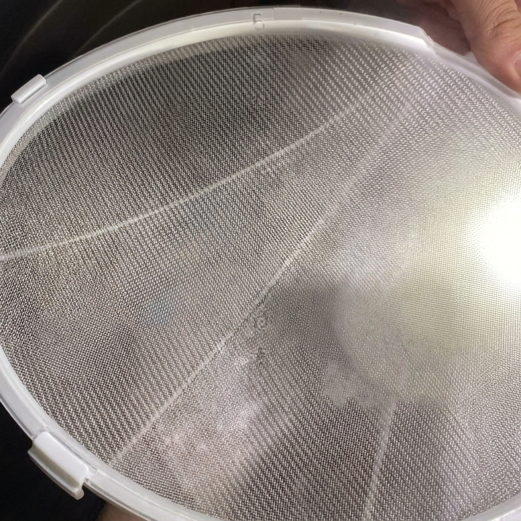 A fine-mesh sieve being held over a pot, with creamy white chicken broth being strained through it.