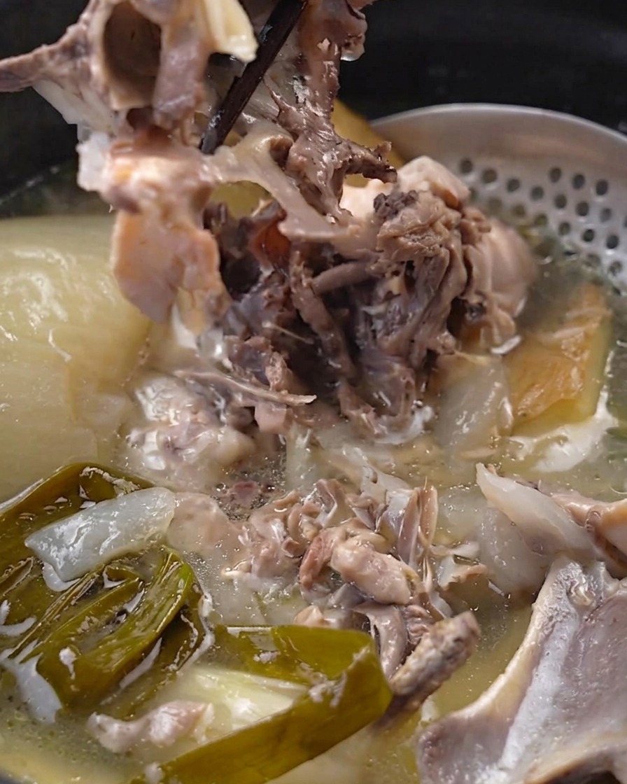Chopsticks separating cooked tender chicken meat from the bone inside the pot