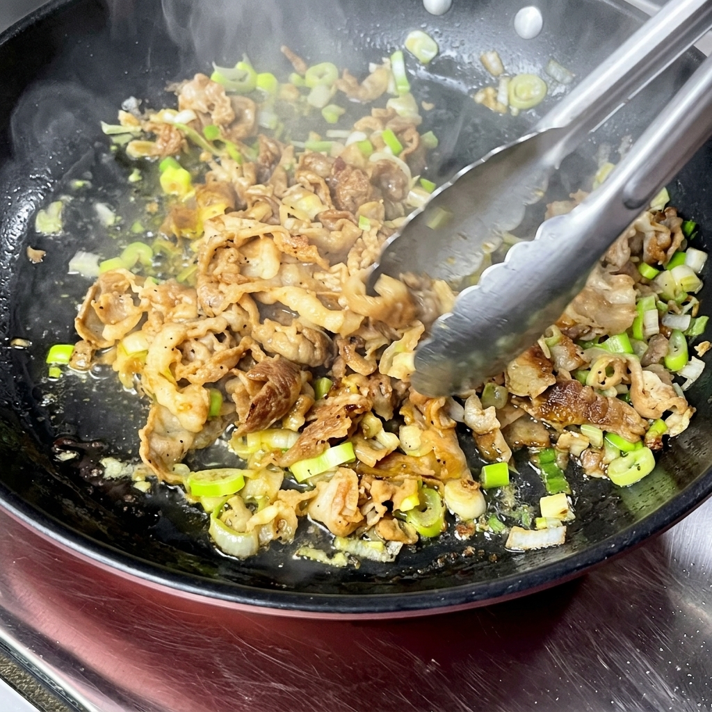 Angus beef slices being stir-fried with scallions in a hot pan using kitchen tongs.