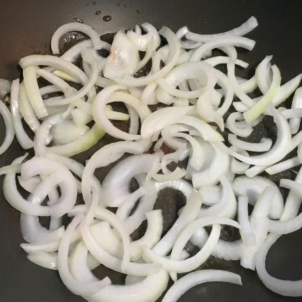 Onion slices cooking in a pan until translucent.