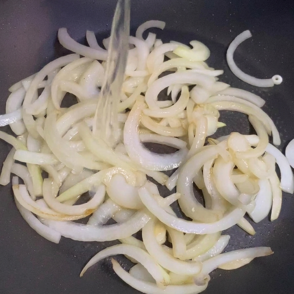 Sake being poured into a pan containing sautéed onions.