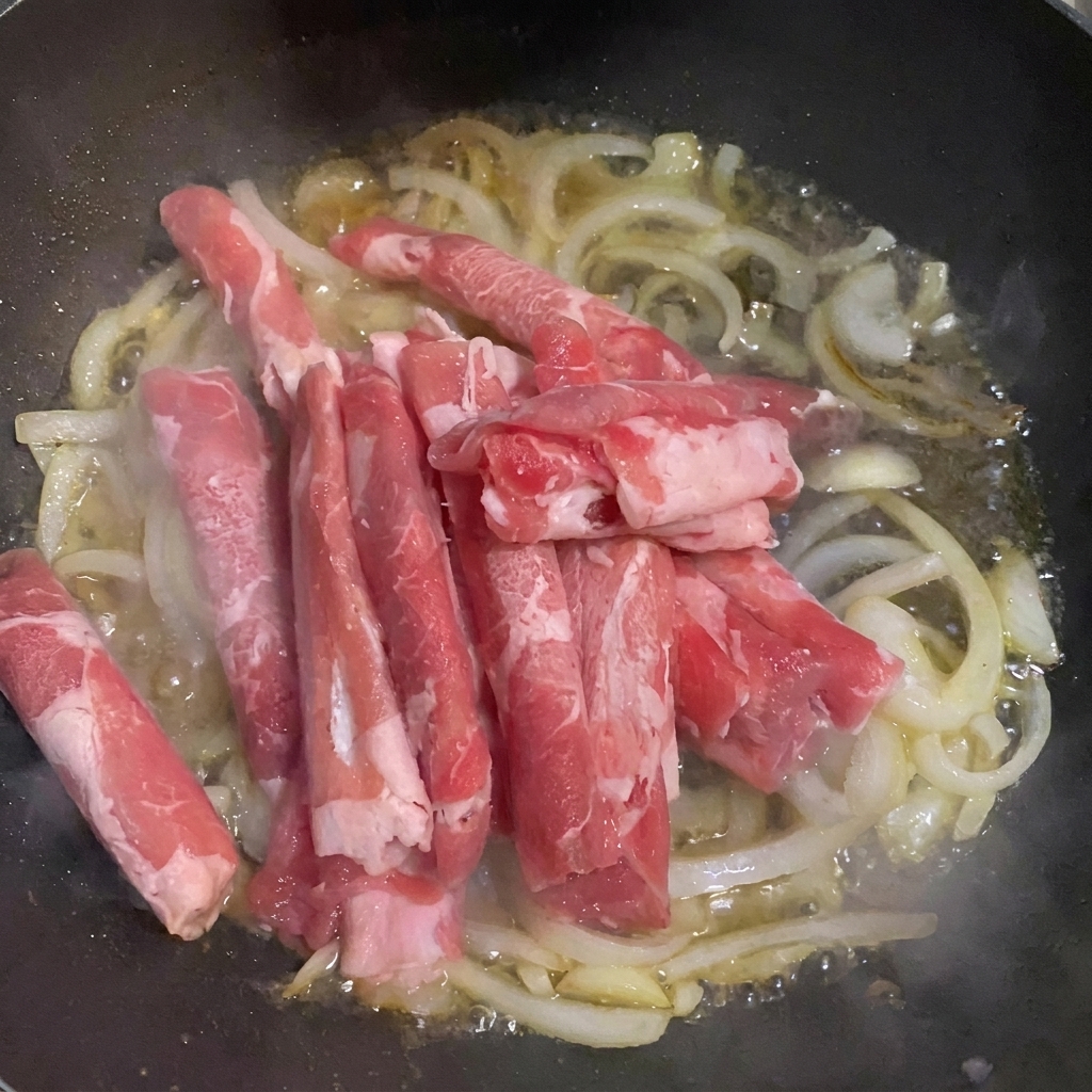 Thin beef slices added to a pan with onions and water.