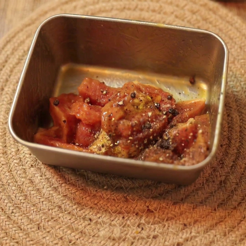 Marinated raw sliced beef seasoned with black pepper and oil resting in a small rectangular container.