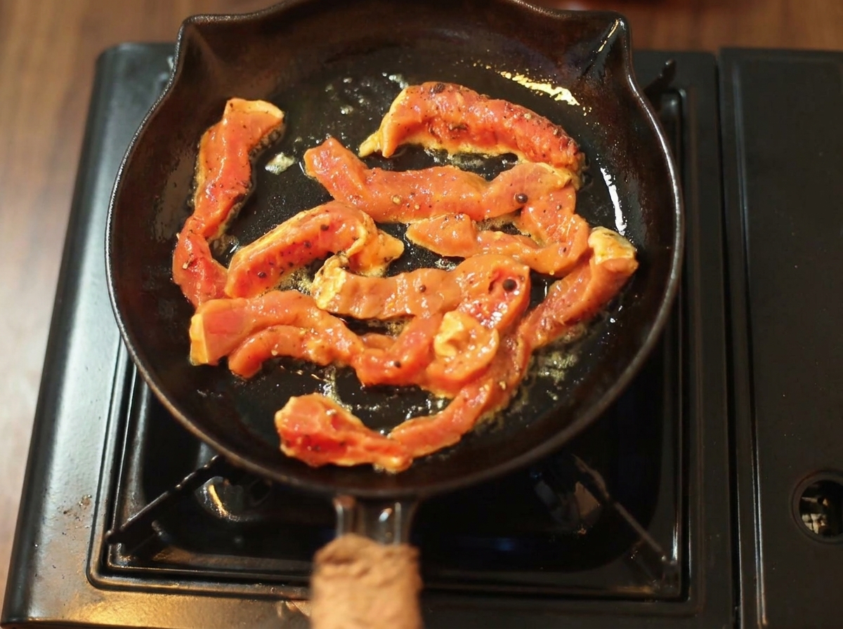 Seasoned beef strips sizzling and browning in a hot black cast-iron skillet.