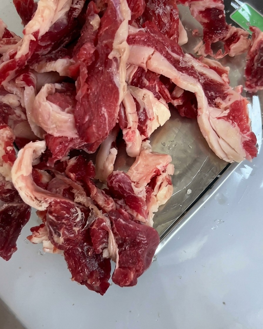 Fresh raw beef chuck pieces neatly arranged in a shallow stainless steel tray.