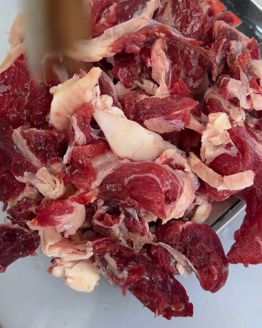Freshly sliced shiitake mushrooms resting on top of the raw beef chuck in a metal tray.