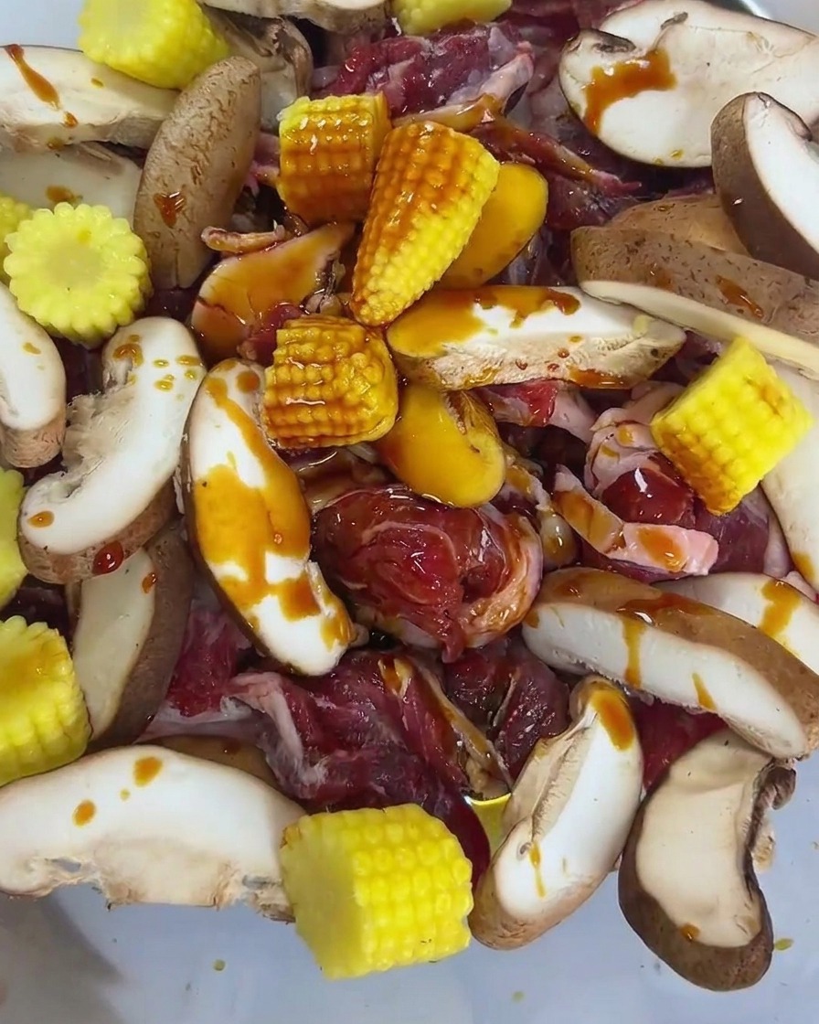 Seafood soy sauce and oyster sauce being poured over the raw beef, mushroom, and baby corn mixture.