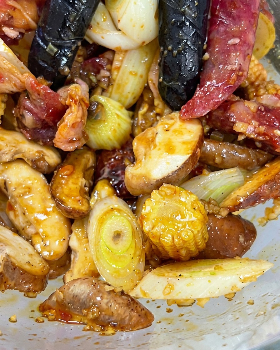 Gloved hands mixing together beef, mushrooms, baby corn, and aromatics in a glass mixing bowl.