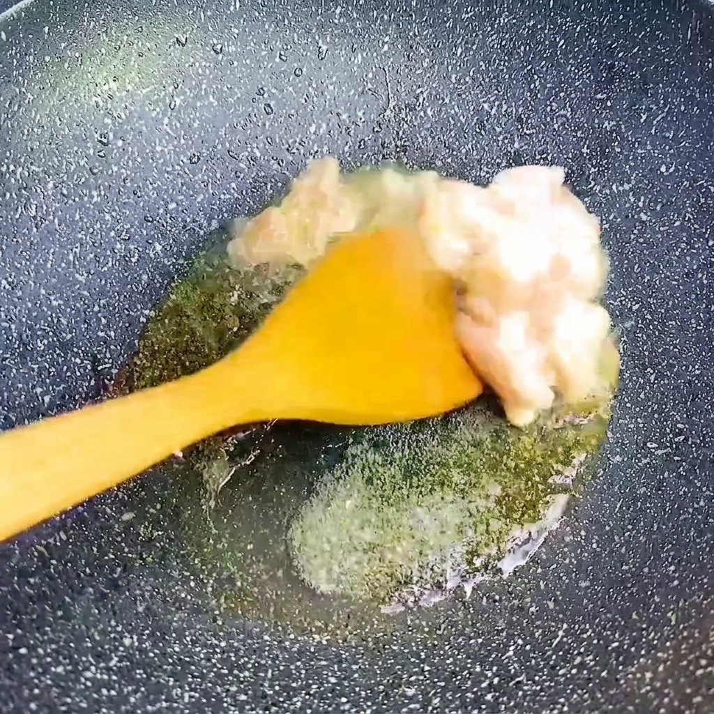 Small chunks of pork belly being stir-fried with a yellow spatula in a hot, dark pan.