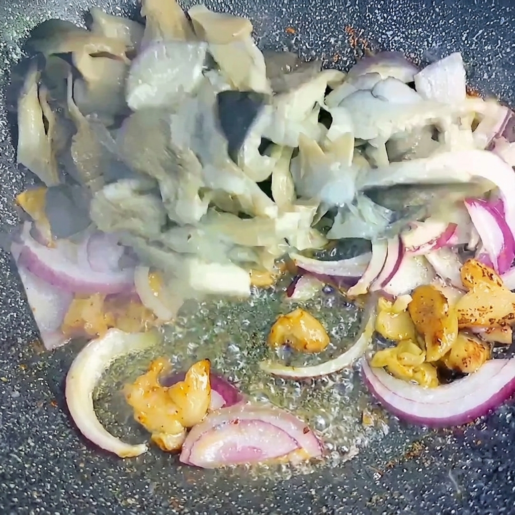 Blanched oyster mushrooms and sliced red onions being tossed together with rendered pork belly pieces in the wok.