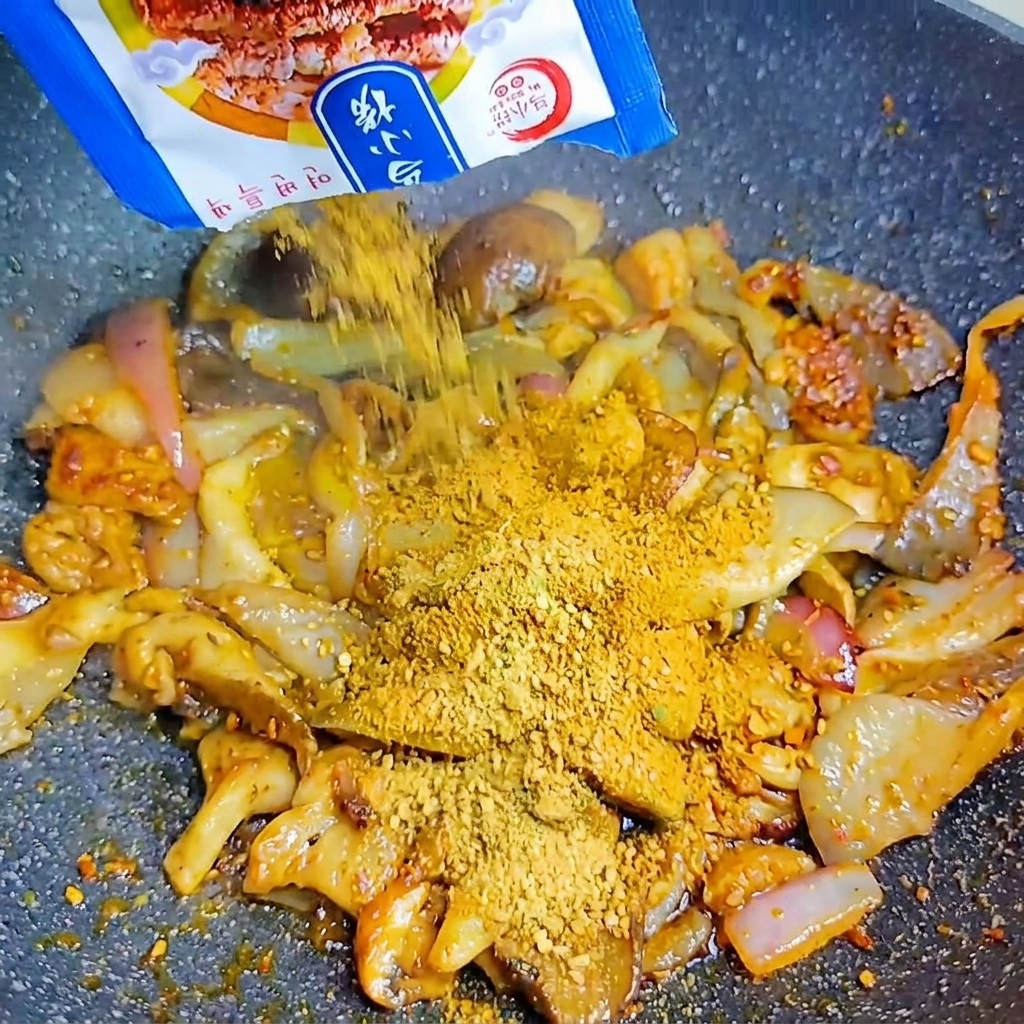 A blue packet pouring Korean BBQ seasoning powder over the mushrooms and onions in the hot wok.