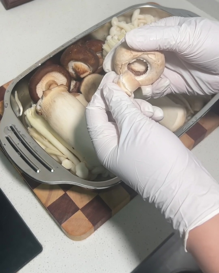 A hand removing the stem from a whole, raw shiitake mushroom cap.