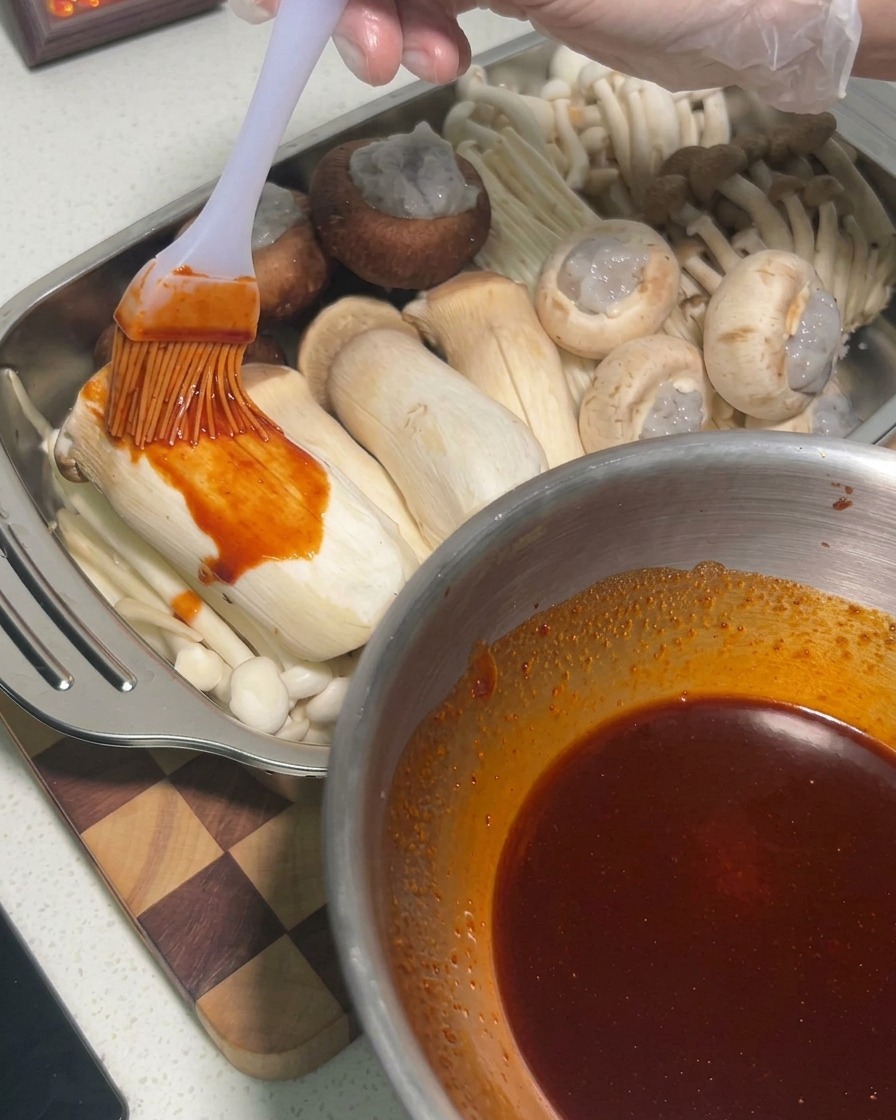 Sauce being brushed onto raw king oyster mushrooms inside a metal tray.