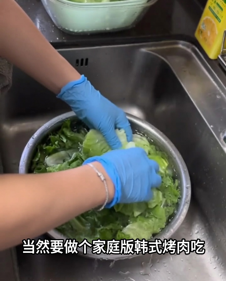 Fresh green lettuce leaves being washed in a large metal bowl filled with water.