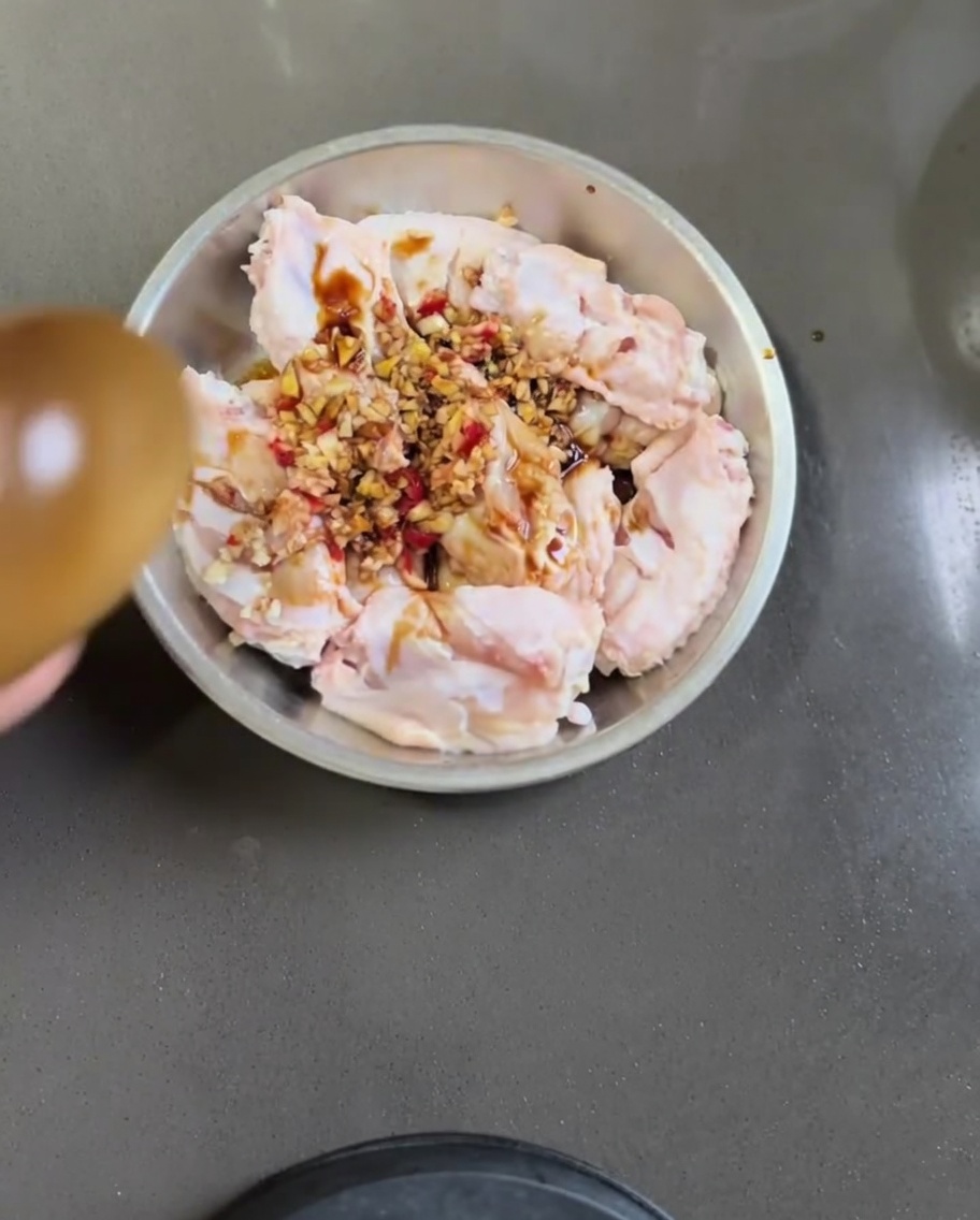 Raw chicken wings in a metal bowl mixed with garlic, chili, soy sauce, and sesame oil.
