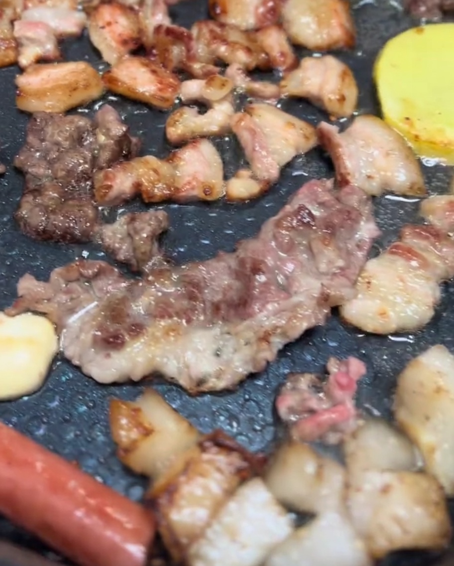 Pork belly, mushroom caps, and potato slices sizzling on an electric grill with a nice golden-brown sear.