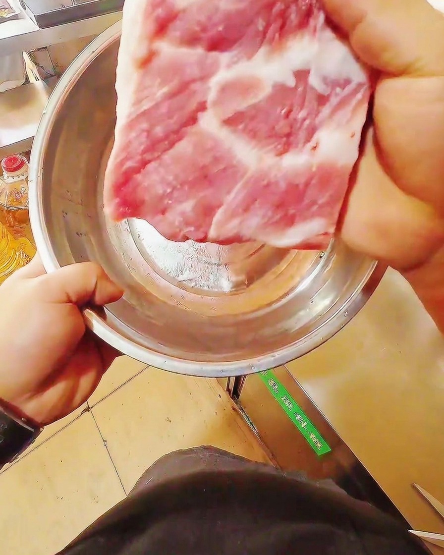 A sharp knife slicing through a fresh, raw slab of pork belly on a wooden cutting board.