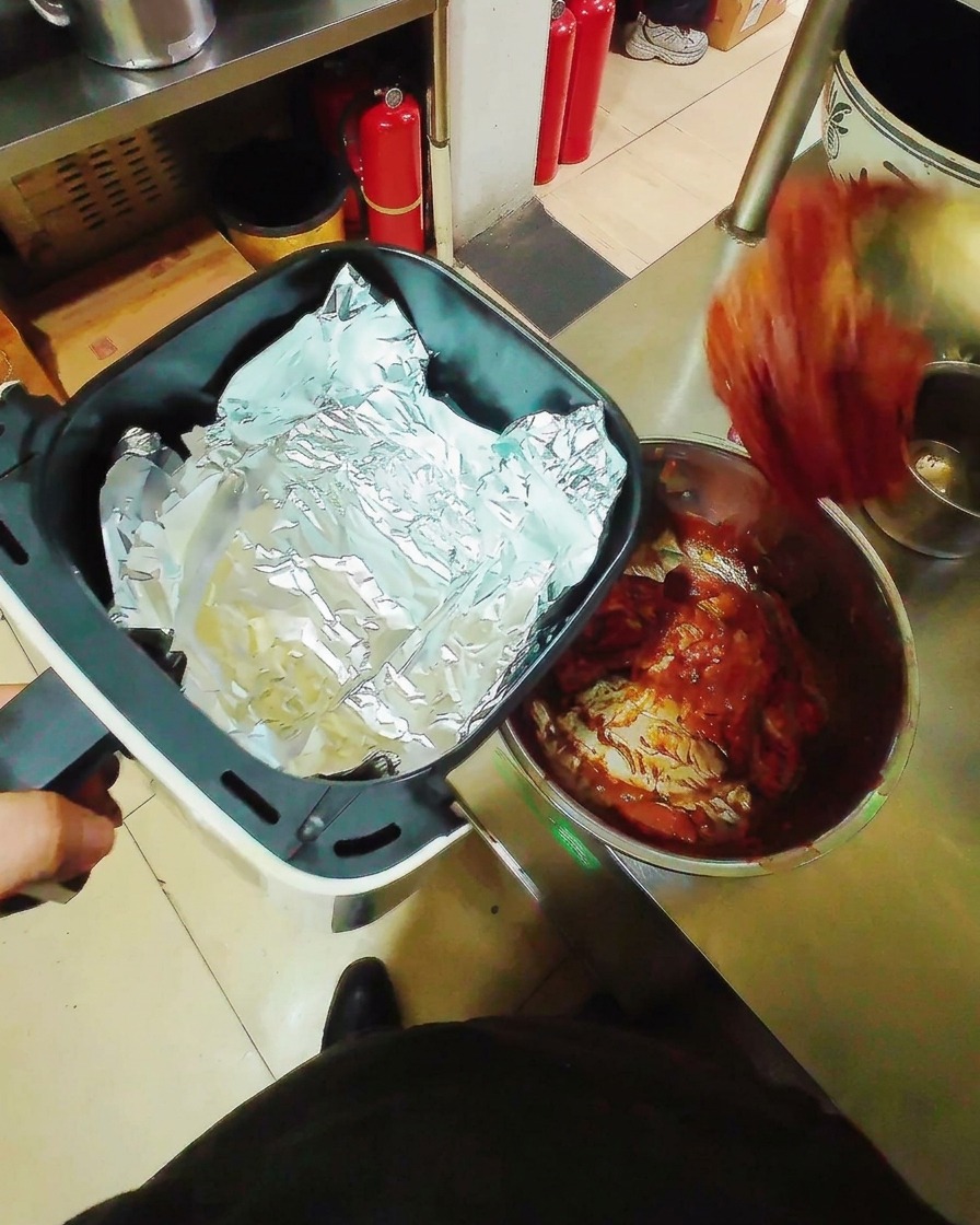 Marinated pork belly strips laid flat on aluminum foil inside an air fryer basket, ready for cooking.