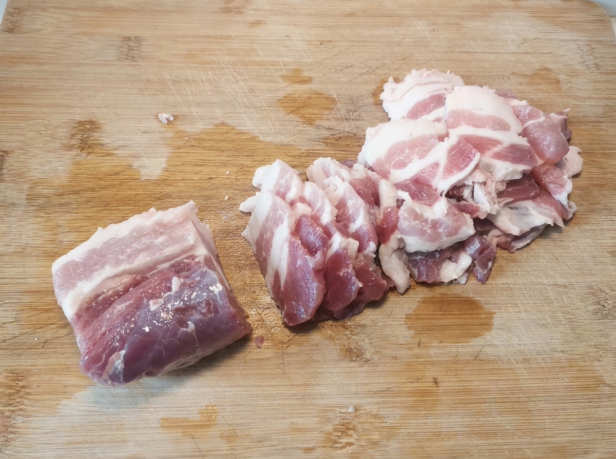 Thin, raw pork belly slices neatly arranged on a wooden cutting board after being cut.