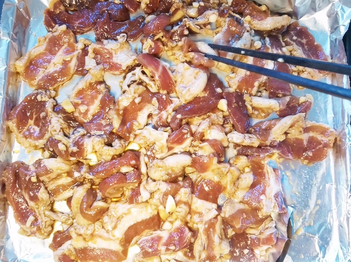 Marinated pork belly slices laid out in a single layer on a foil-lined baking tray.
