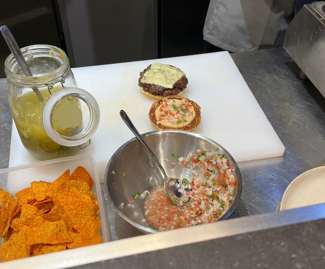 Ground beef patties being smashed thin on a hot griddle with a metal press.