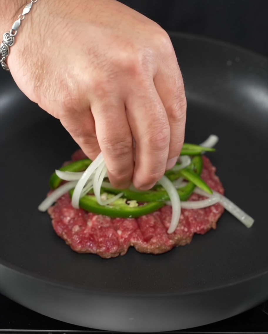 Fresh jalapeño rings and onion slices placed atop a sizzling beef patty.
