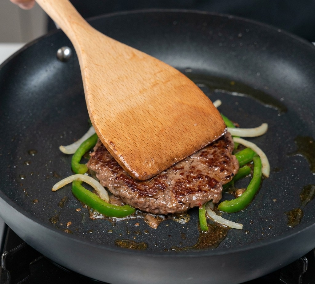 A slice of cheddar cheese resting on top of a beef patty covered with jalapeños and onions.