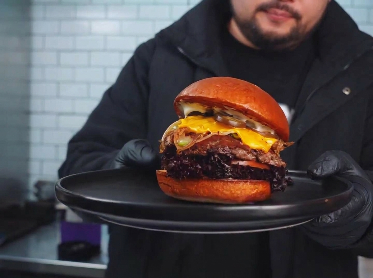 A seared beef patty on the grill topped with stir-fried vegetables and a slice of melting cheese.