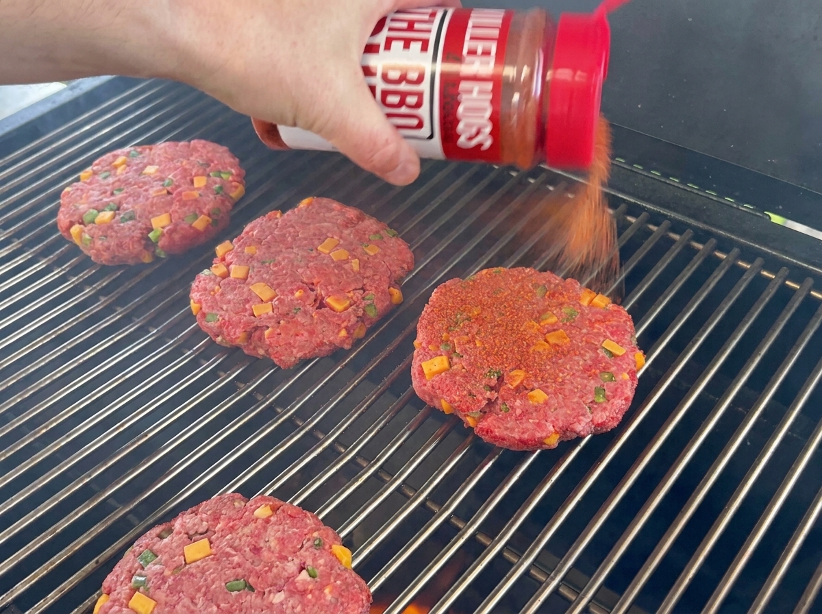 Beef patties seasoned with BBQ rub resting on grill grates.