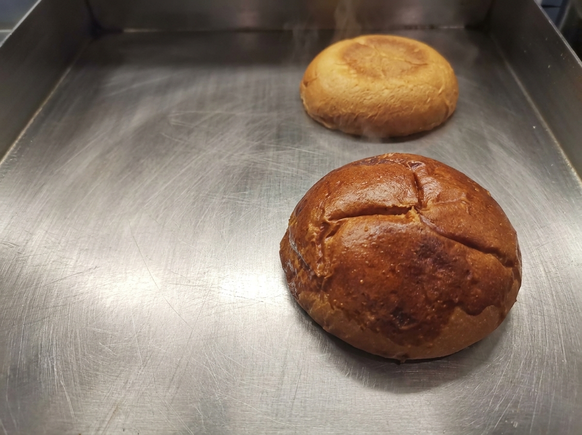 Golden brown toasted burger bun halves resting on a clean griddle surface.